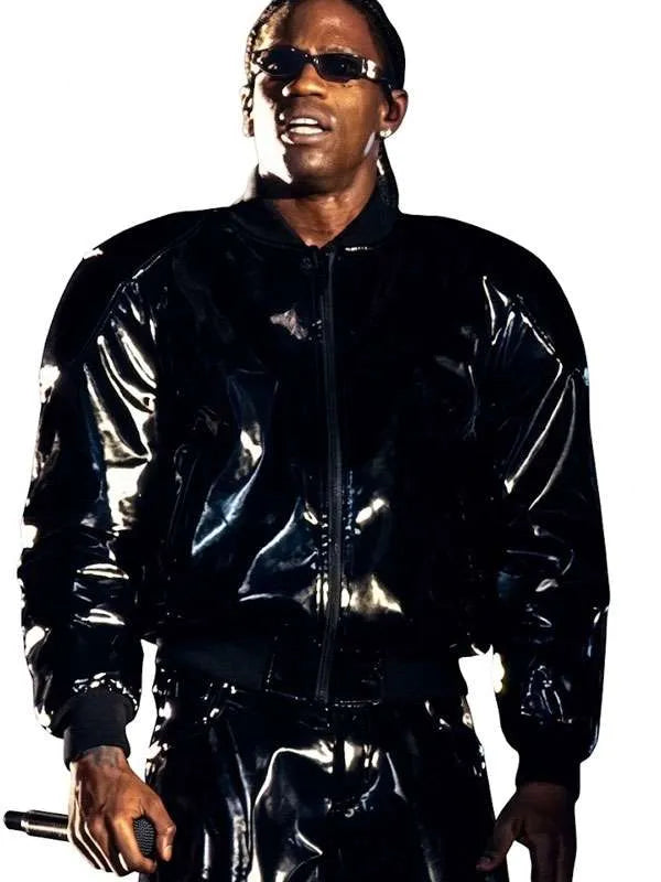 A man wearing a shiny black patent leather bomber jacket and matching pants, with black sunglasses, posed against a solid white background.