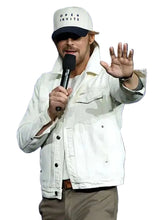 Person wearing a white cap and jacket, holding a microphone against a blue background