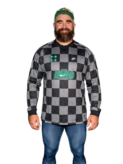 Man wearing a checkered shirt with visible branding, standing in front of a dark background.