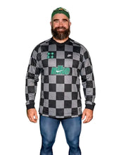 Man wearing a checkered shirt with visible branding, standing in front of a dark background.