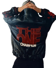 A person viewed from behind wearing a black leather jacket with large red and white text on the back reading 'THE ONE CHAMPION' and red sleeve graphics, standing indoors against a brown wall.