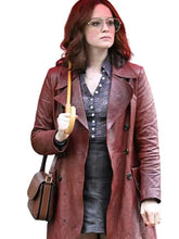 A woman with red hair wearing aviator sunglasses, a reddish-brown leather trench coat over a patterned blouse and dark skirt, holding a brown handbag and umbrella against a plain white background.