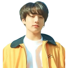 A close-up portrait of a young man wearing a yellow-orange jacket with a dark collar over a white t-shirt, set against a bright blue background.