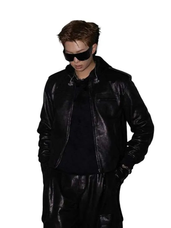 A man wearing a black leather jacket, black pants, and black sunglasses, standing against a solid white background.