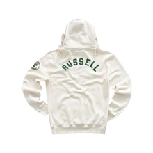 An off-white hooded sweatshirt shown from the back, featuring 'RUSSELL' printed in dark green arched block letters across the upper back and a small circular patch on the left sleeve, set against a solid light gray background.