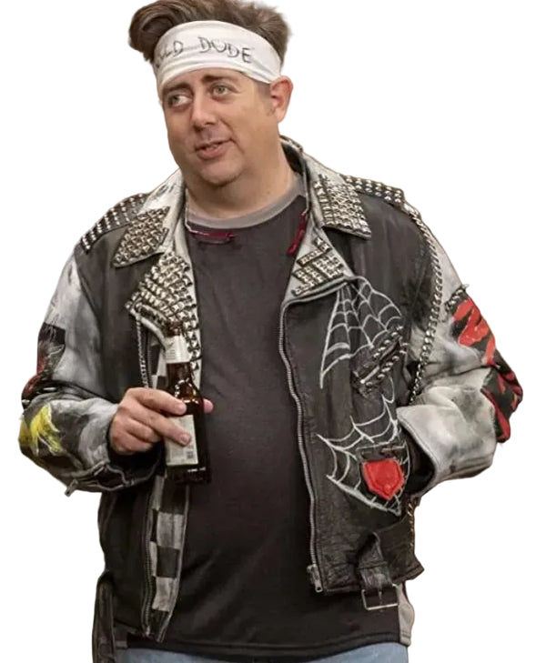 A man wearing a heavily embellished black leather jacket with silver studs, a spiderweb graphic on the front, a red rose patch on the sleeve, a white headband with 'HELLO DUDE' written on it, and holding a beer bottle in a kitchen setting.