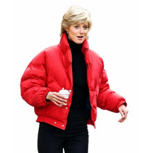 A woman wearing a bright red cropped puffer jacket over a black turtleneck and black pants, holding a takeaway coffee cup against a plain white background.