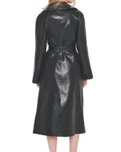A woman viewed from the back wearing a black faux-leather coat with a matching waist belt, set against a plain light gray studio background.