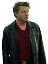 A man wearing a black leather jacket over a red and black vertically striped V-neck sweater, shown from the chest up against a plain light gray background.