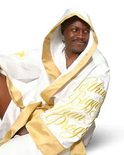 A man wearing a white hooded robe with gold trim and gold script text reading 'Nothing Bigger than my Progress' on a plain white background.