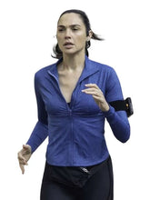 A woman running outdoors wearing a blue long-sleeve zip-up athletic top and black running pants, with a black armband phone holder on her upper arm.