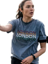 A woman wearing a heathered slate blue graphic T-shirt with 'LONDON' printed across the chest in layered multicolor text, photographed against a plain white background.