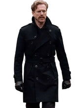 A man wearing a long black double-breasted trench coat with a matching belt, black gloves, and a mustache, isolated on a white background.