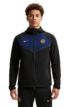 A man wearing a black Nike Inter Milan track jacket with blue and gold panels, featuring the Inter Milan club crest and Nike swooshes, set against a plain light gray background.