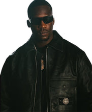 A man wearing a black leather jacket with a visible Stone Island badge on the pocket and dark sunglasses, shown against a plain white background.