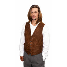 A man with long brown hair wearing a brown suede vest over a white long-sleeve shirt and gray trousers, standing against a plain white background.