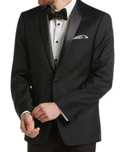 A man wearing a black tuxedo jacket with satin peak lapels, a white dress shirt, a black bow tie, and a patterned pocket square, photographed against a light gray studio background.