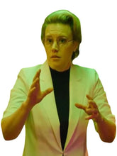 A cropped portrait of a person with short light hair, wearing a white blazer over a black top and glasses, with hands raised in a gesturing pose against a plain white background.