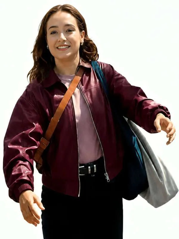 A woman wearing a shiny burgundy bomber jacket over a mauve top and black pants, carrying a brown shoulder bag and a blue-gray tote bag against a plain white background.