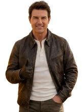 A man wearing a distressed brown leather jacket over a white henley shirt, standing against a plain white background and giving a thumbs-up.
