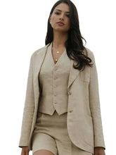 A woman modeling a light beige linen three-piece suit consisting of a blazer, button-front vest, and matching shorts, set against a plain white background.