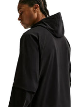 A side profile view of a person wearing a black hooded jacket against a light gray background.