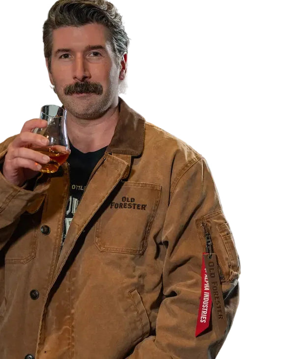 A man with a mustache wearing a brown Old Forester work jacket and holding a glass of amber liquid, set against a dark, industrial background.
