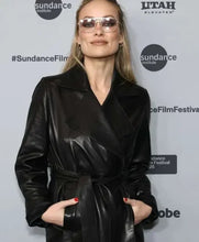 A woman wearing a black leather wrap coat and clear aviator-style sunglasses stands in front of a Sundance Film Institute backdrop with Utah Elevated branding.