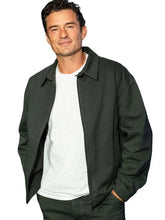 A man wearing a dark charcoal gray zip-up jacket over a white t-shirt and dark pants, photographed against a solid white background.