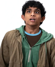 A young man with curly dark hair wearing a brown zip-up jacket over a green hoodie and a brown t-shirt with a light blue collar, looking upwards with a surprised expression against a white background.