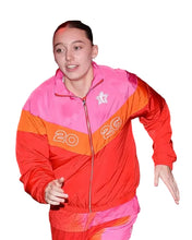 A person wearing a bright color-blocked zip-up jacket and matching pants in pink, orange, and red, photographed in a crowded indoor event setting.