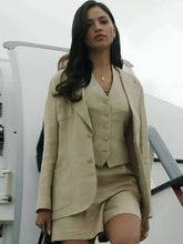 A woman wearing a matching beige three-piece suit consisting of a blazer, vest, and shorts, standing on the steps of an aircraft.