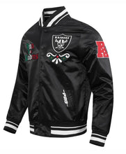 A black satin bomber jacket featuring Oakland Raiders patches, including the Raiders logo on the chest, a 'Raiders vs. Cowboys' patch on the right sleeve, and a red 'A' patch on the left sleeve, shown against a plain white background.