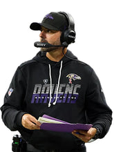 A man wearing a black Baltimore Ravens hoodie with 'DAIENCE ENGINEERED FOR' text, a black cap, and a Sony headset, holding purple folders against a light gray background.