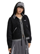 A model wearing a black Adidas zip-up jacket with gray trim, a gray headband, and a gray skirt with white stripes, set against a solid light gray background.
