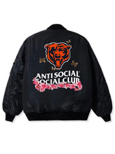 Black bomber jacket shown from the back, featuring a large orange bear head graphic, the text 'ANTI SOCIAL SOCIAL CLUB' in white, and a pink floral design with butterflies.