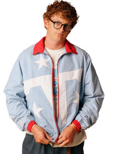 A man wearing a light blue windbreaker jacket with a white graphic print and red collar, cuffs, and zipper trim, styled over a white t-shirt and dark pants.