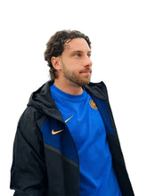 A man wearing a blue Inter Miami CF soccer jersey under a black and blue Nike jacket, standing in front of an airplane doorway.