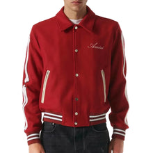 A red varsity-style jacket with white stripe details on the sleeves and hem, featuring a white script logo on the left chest, worn by a model.