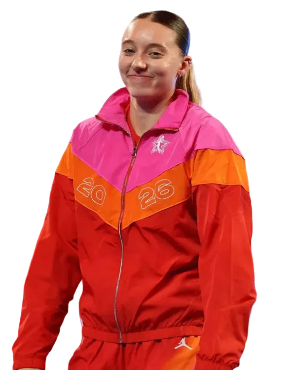 A woman wearing a bright red, orange, and pink zip-up athletic jacket with the number 26 on the front, standing on a stage-like setting.