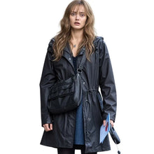 A woman wearing a black hooded raincoat with a drawstring waist, a black crossbody bag, and holding a blue folder against a plain white background.