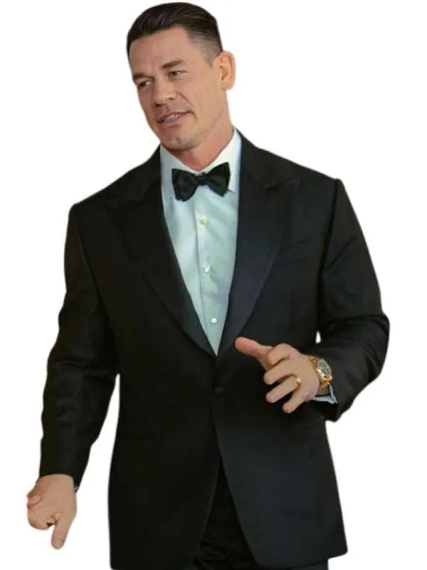 A man wearing a black tuxedo jacket with black satin lapels, a black bow tie, and a light blue dress shirt, posed against a plain white background.