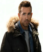 A man wearing a black winter parka with a beige faux-fur hood lining, layered over a blue denim shirt and a gray t-shirt, set against a plain white background.