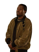 A man wearing a brown suede bomber jacket with black star details on the sleeves, styled over a black shirt, photographed against a solid white background.