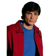 A young man with dark hair and blue eyes wearing a red jacket over a blue t-shirt, standing in front of a rustic wooden door.
