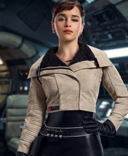 A woman wearing a beige cropped jacket with a black fuzzy collar, black gloves, and a black skirt, standing in a futuristic interior setting.