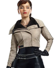 A woman modeling a cropped beige faux-leather jacket with a black fuzzy collar, paired with a black belt, black skirt, and black gloves, against a plain white background.