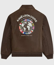 A brown leather bomber jacket shown from the back, featuring a large graphic print with the text 'AIMÉ LEON DORE', a globe design, and various national flags on a light gray background.