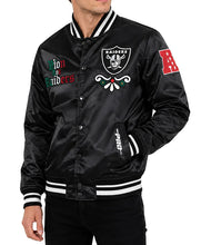 A man wearing a black satin Oakland Raiders varsity jacket with embroidered patches, including the Raiders shield on the chest, 'Raiders' on the sleeve, and 'Lion to Raiders' on the opposite chest, against a white background.