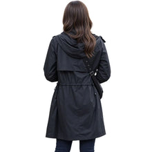A woman viewed from behind wearing a black hooded trench coat with a drawstring waist and a black shoulder bag, set against a plain white background.